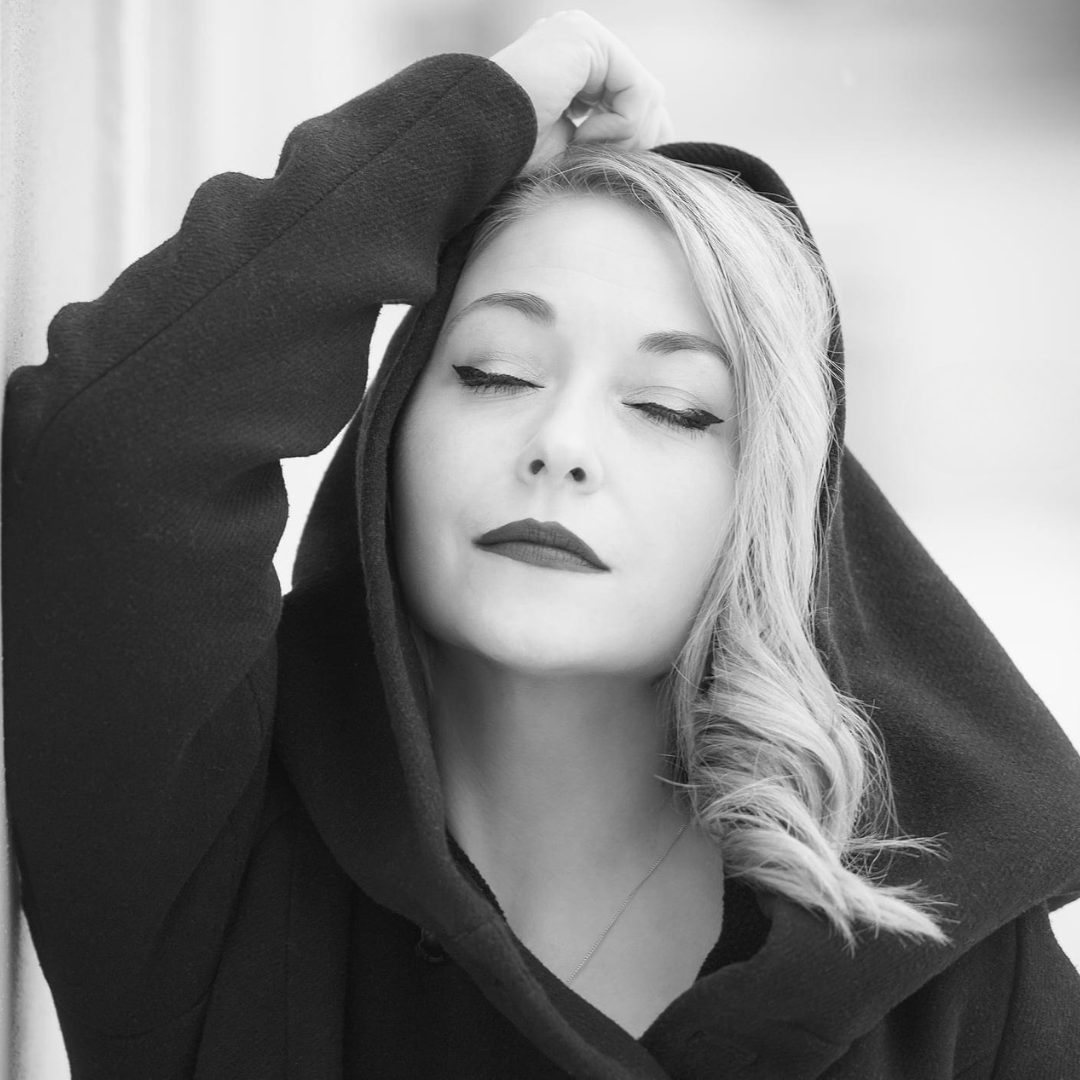 Schwarzweiß-Portrait einer attraktiven Frau mit geschlossenen Augen, outdoor fotografiert, sanftes Licht und natürliche Umgebung im Hintergrund.