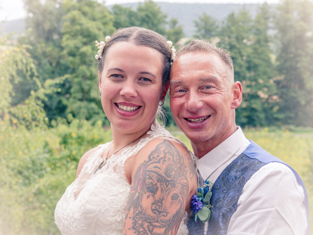 Brautpaar sitzt eng umschlungen beim After-Wedding-Shooting vor Naturhintergrund – Hochzeitsfotografie im Grünen